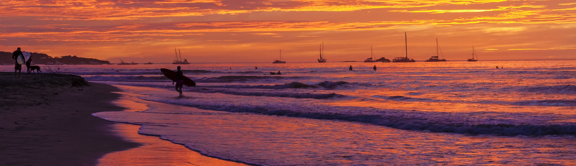 A surfer silhouetted against a brilliantly colored setting sun on Playa Tamarindo
